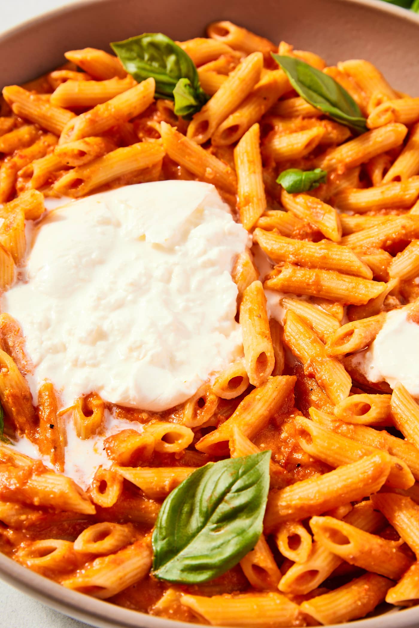 Brown bowl filled with roasted tomato pasta with ball of burrata and fresh basil leaves.