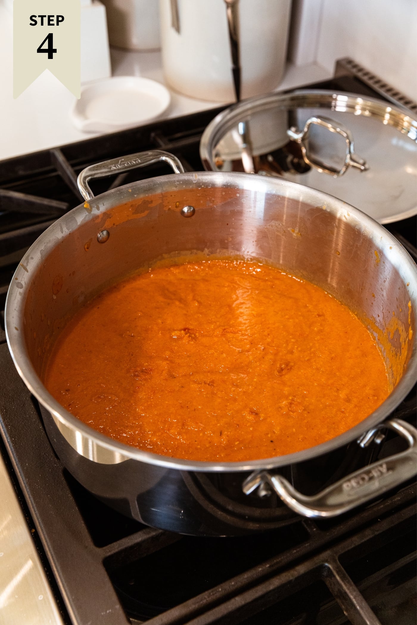Large kettle filled with orange colored tomato sauce heating on the stovetop.