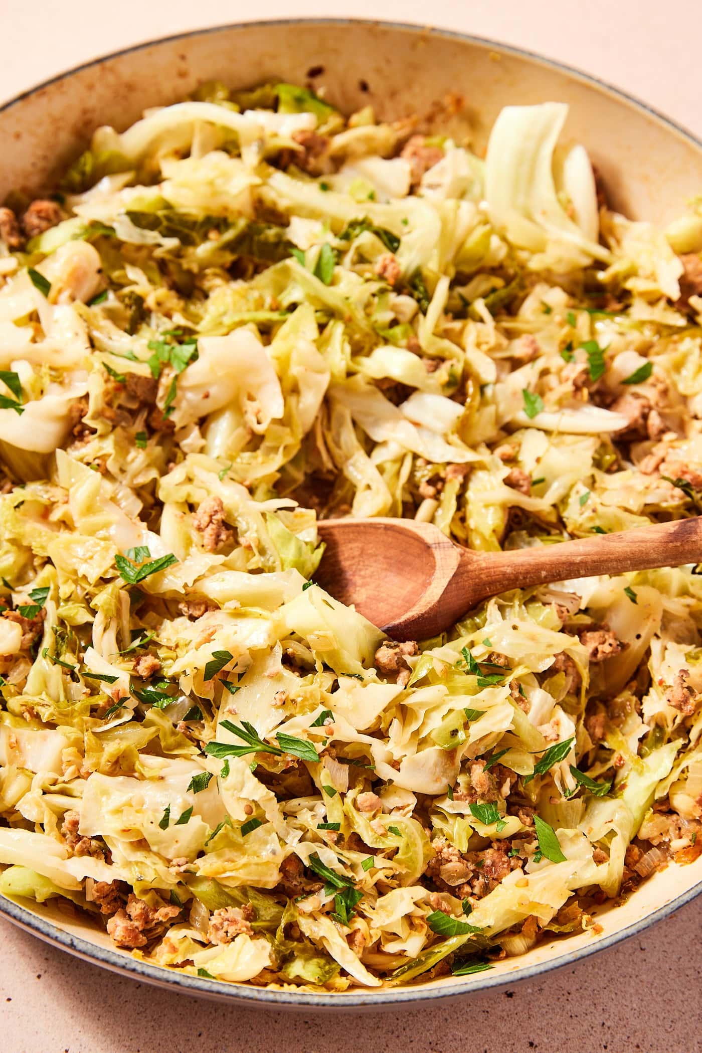 Large gray skillet filled with cooked cabbage and sausage with wooden spoon resting in pan.