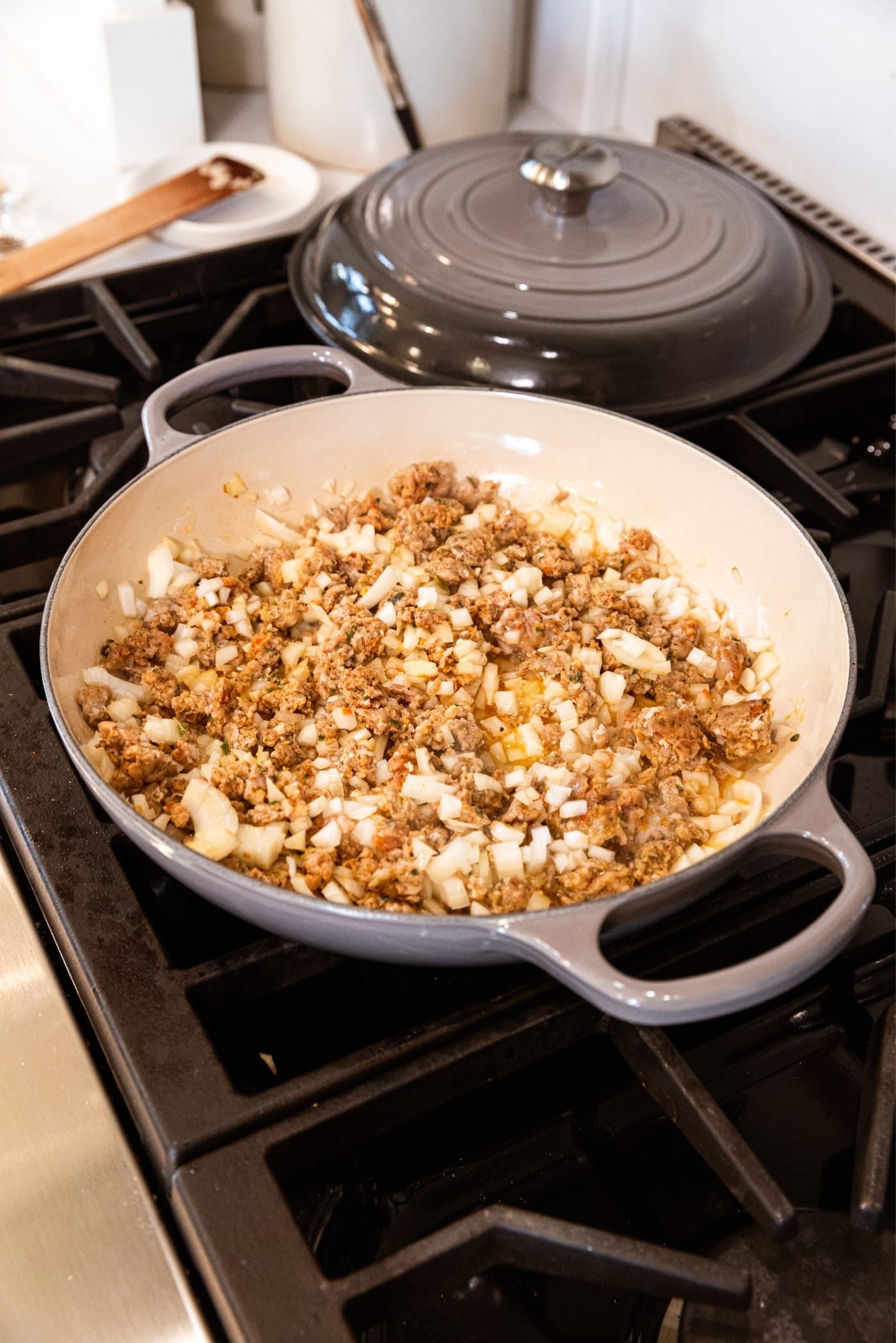 Large skillet on stovetop with cooking mixture of ground sausage and onion and garlic.