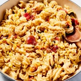Large cooking pot filled with sweet corn pasta with pieces of cooked cherry tomato and wooden spoon resting against the side of the bowl.