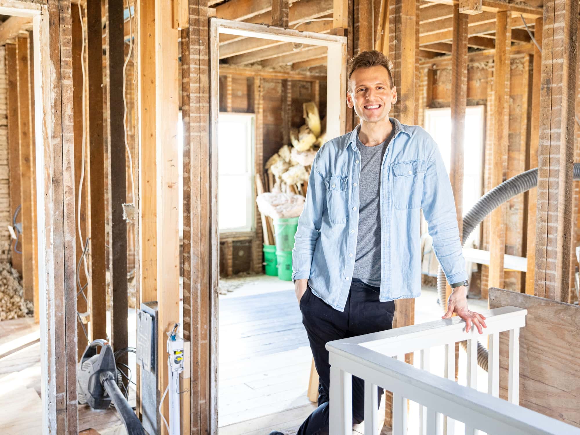 Kaleb Wyse wearing blue shirt standing on second floor with railing and demolished walls during renovation.
