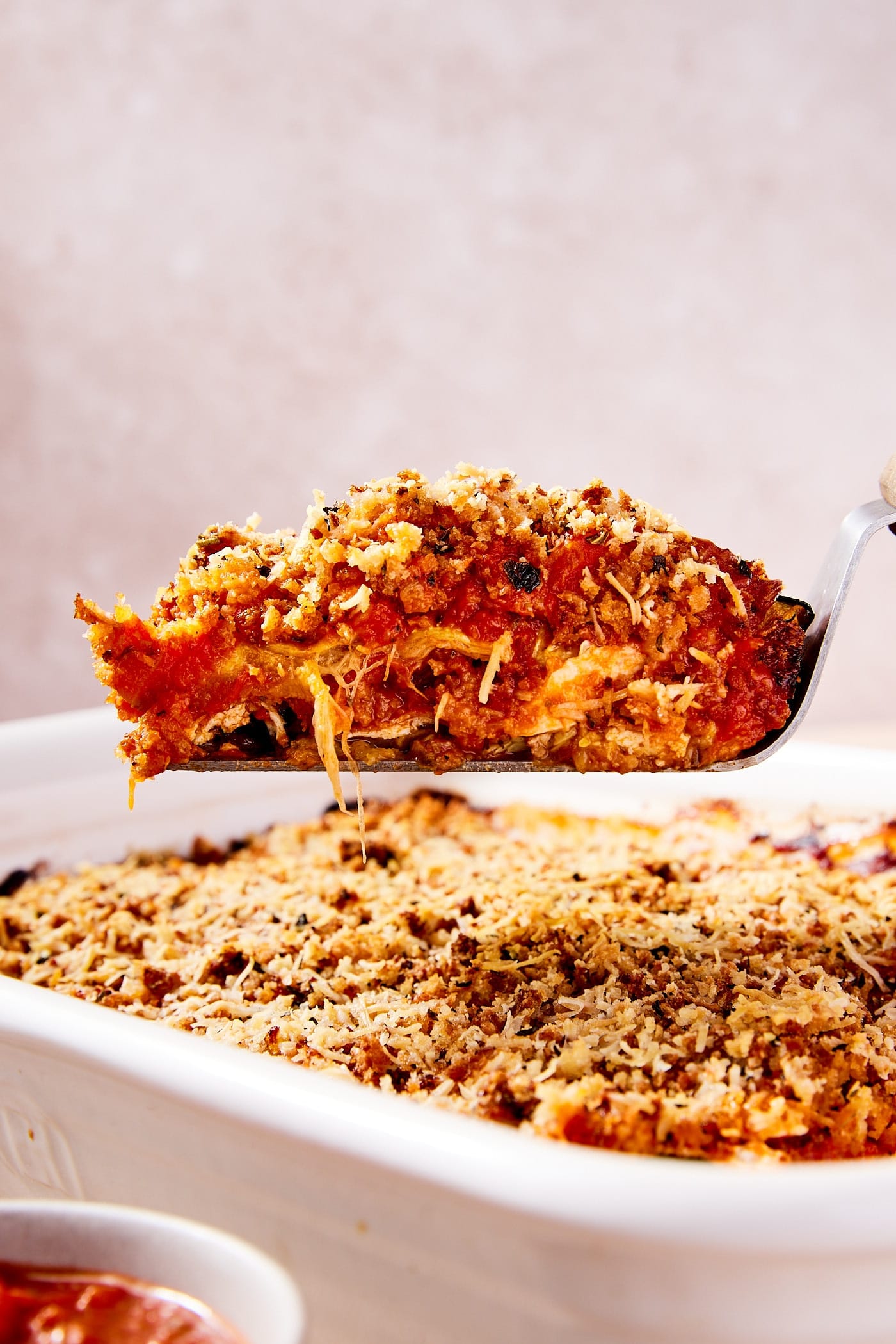 Offset spatula holding a serving of zucchini parmesan showing the interior layers of the dish with rest of casserole sitting below.