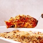 Offset spatula holding serving of zucchini parmesan showing interior layers with rest of casserole below.