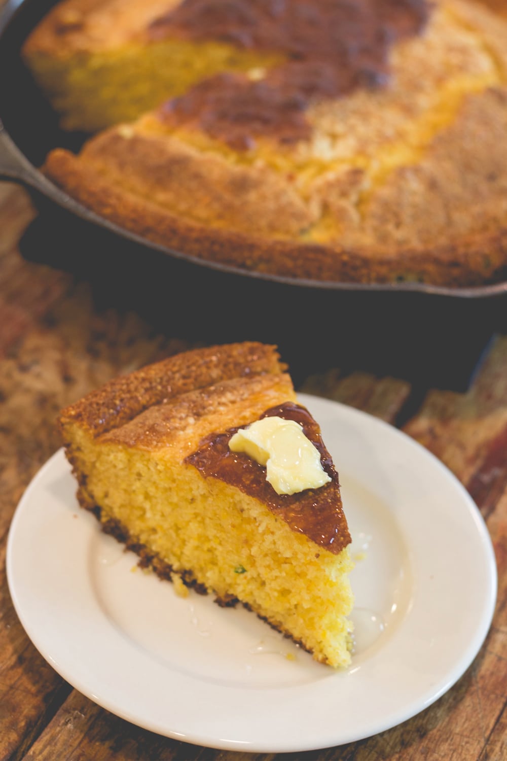 A slice of cornbread topped with butter sits on a plate.