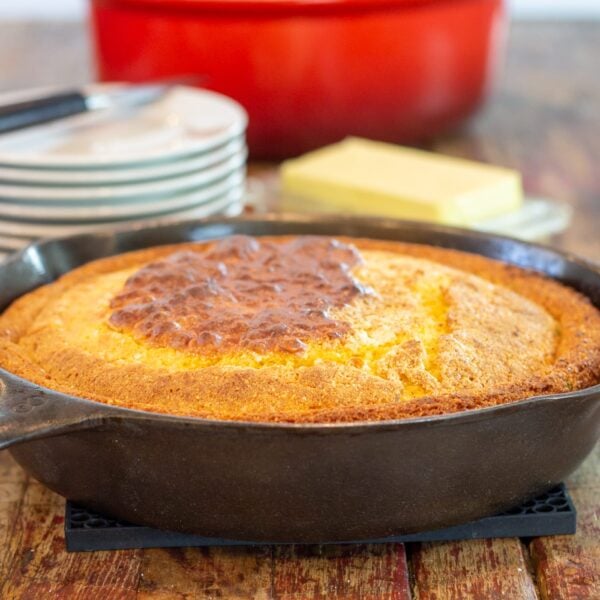 A large skillet filled with cornbread sits in front of dinner plates on a table.