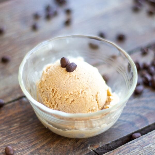 A scoop of ice cream topped with coffee beans sits in a glass dish on a table.