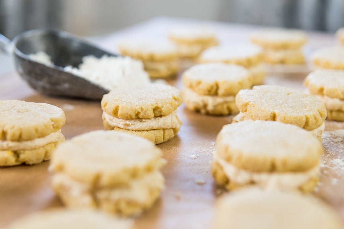 Cookies filled with buttercream scatter across a table.
