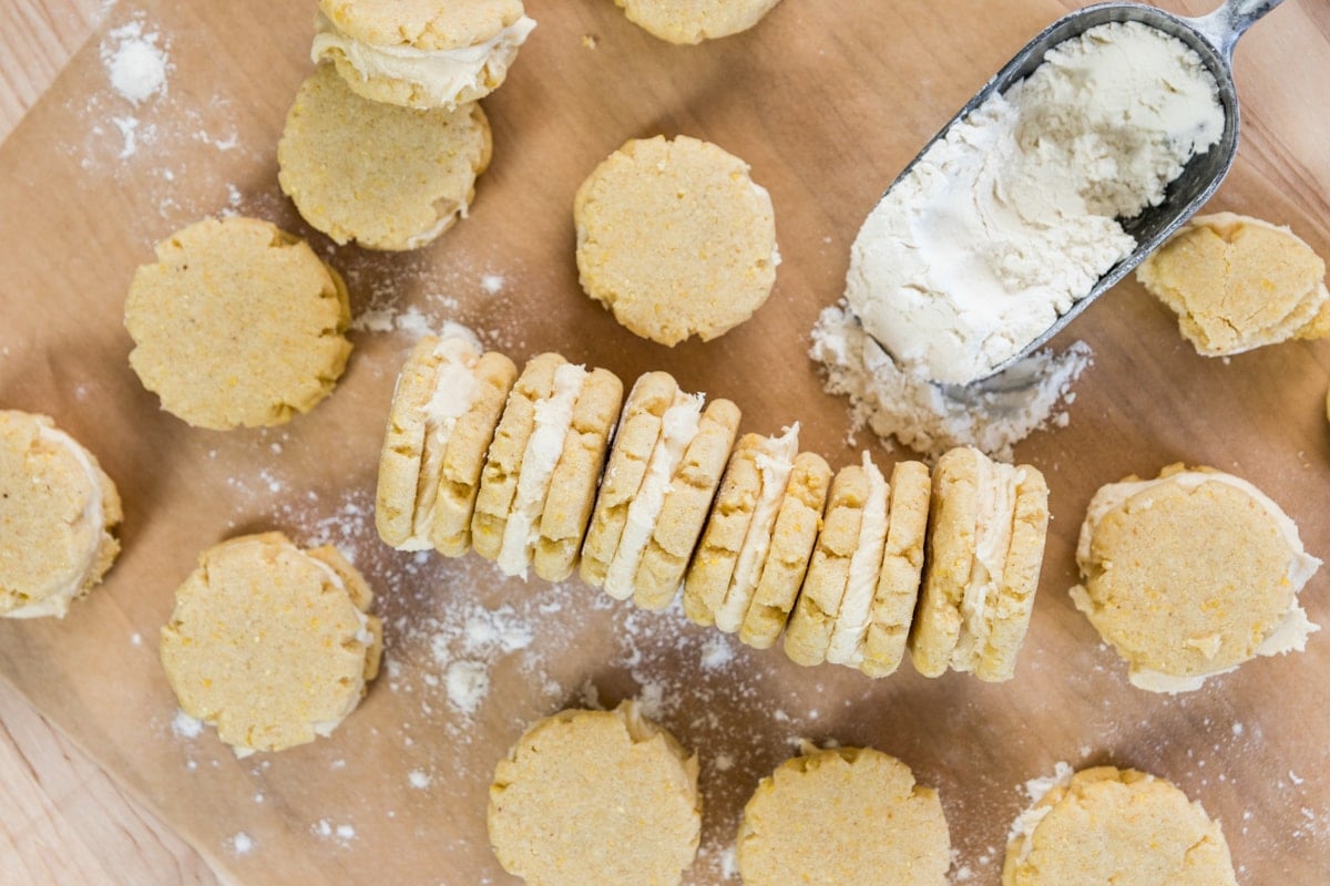 A row of layered cookies sits on parchment with other cookies and flour scattered around.