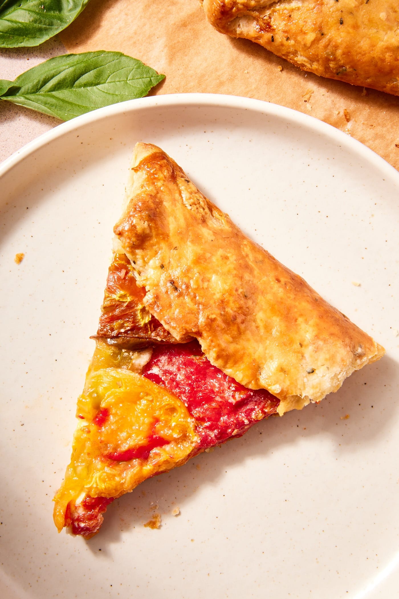 Slice of fresh tomato galette sitting on white plate with flaky browned crust.