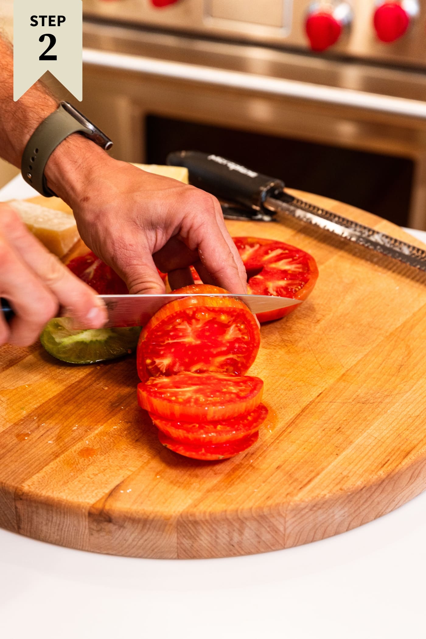 Knife slicing tomato into slices on wood cutting board with more tomatoes in background.