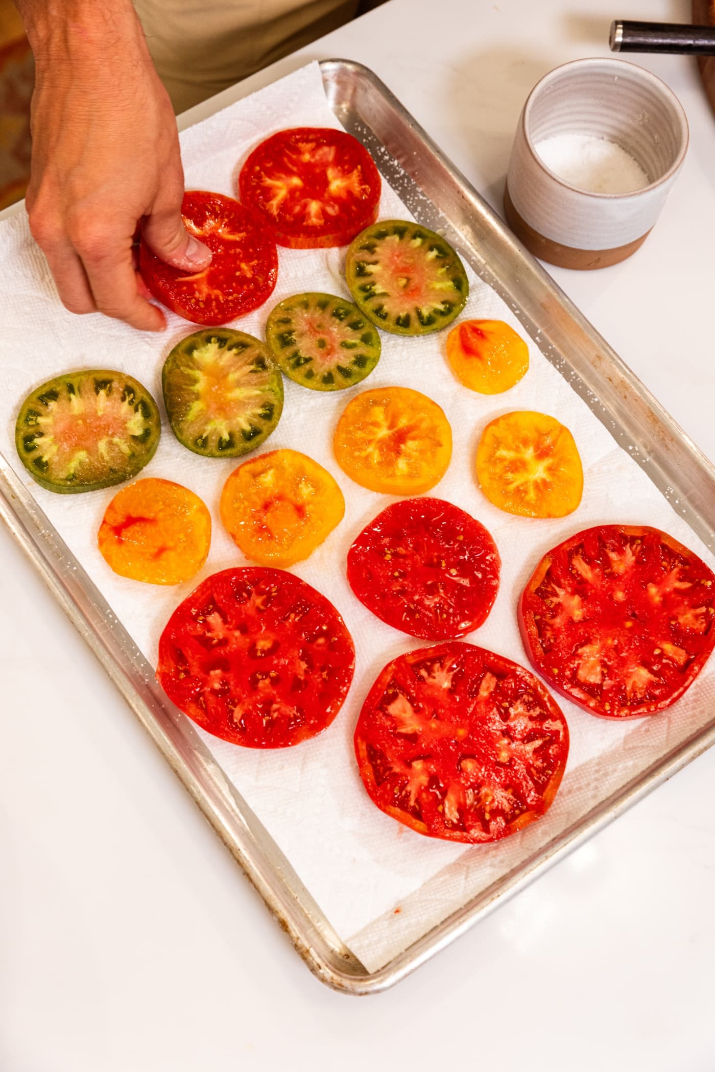 Slices of tomato sitting on pieces of paper towel on a baking sheet.