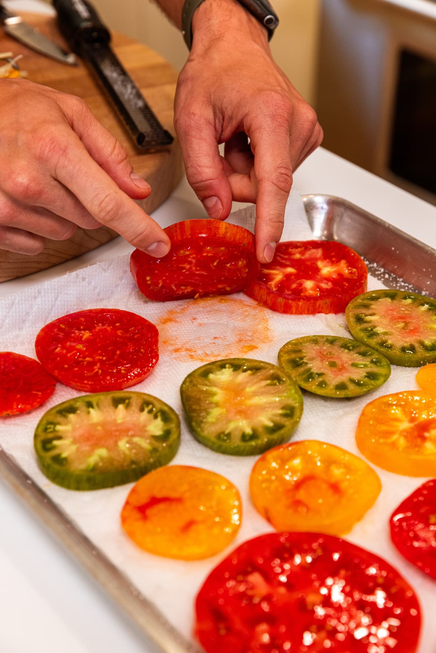 Hand holding slice of tomato up from paper towel showing the wet liquid that seeped out from tomato.