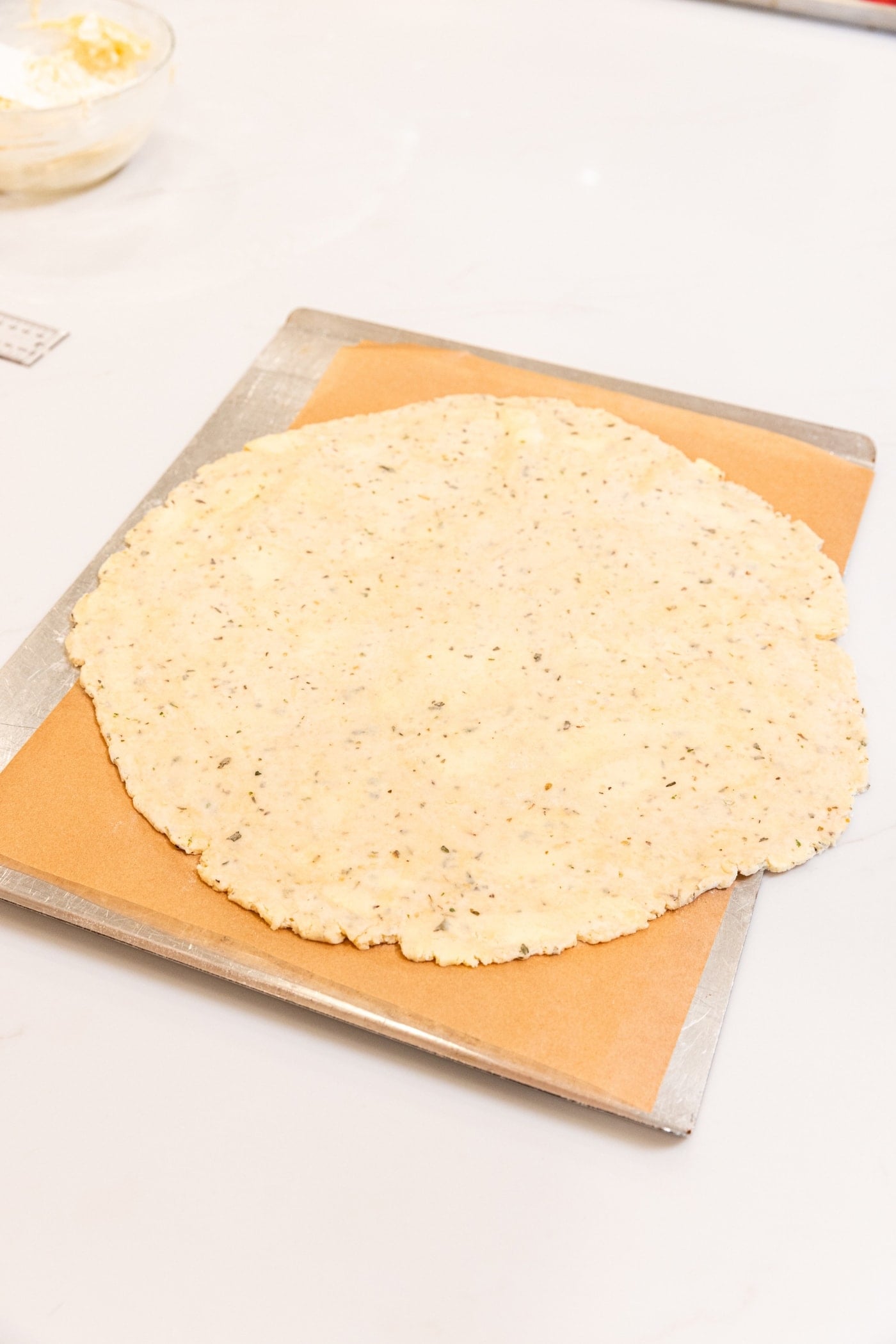 Rolled out piece of dough sitting on parchment-lined baking sheet before being baked.