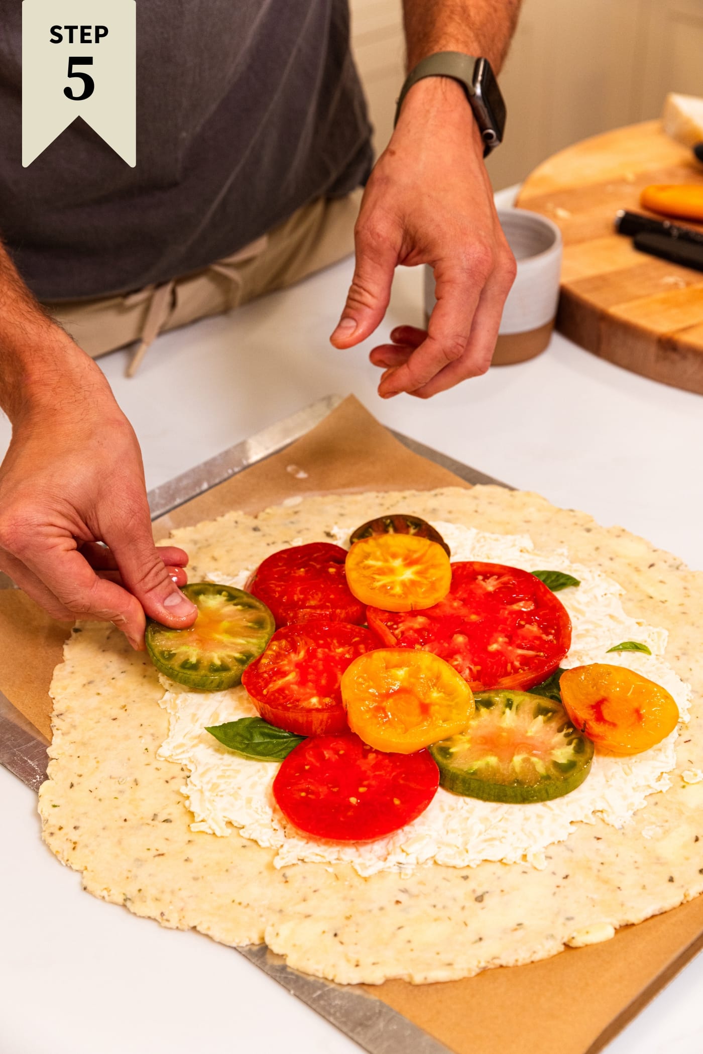 Hand placing slices of tomatoes on top of cream cheese mixture on unbaked dough.
