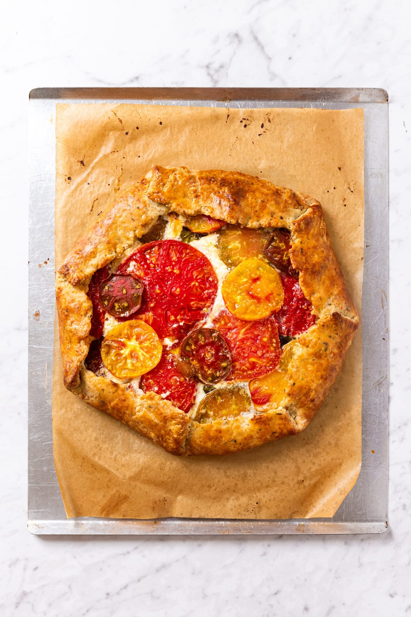 Baked tomato galette with golden brown edges sitting on piece of parchment paper on baking sheet right after coming out of the oven.