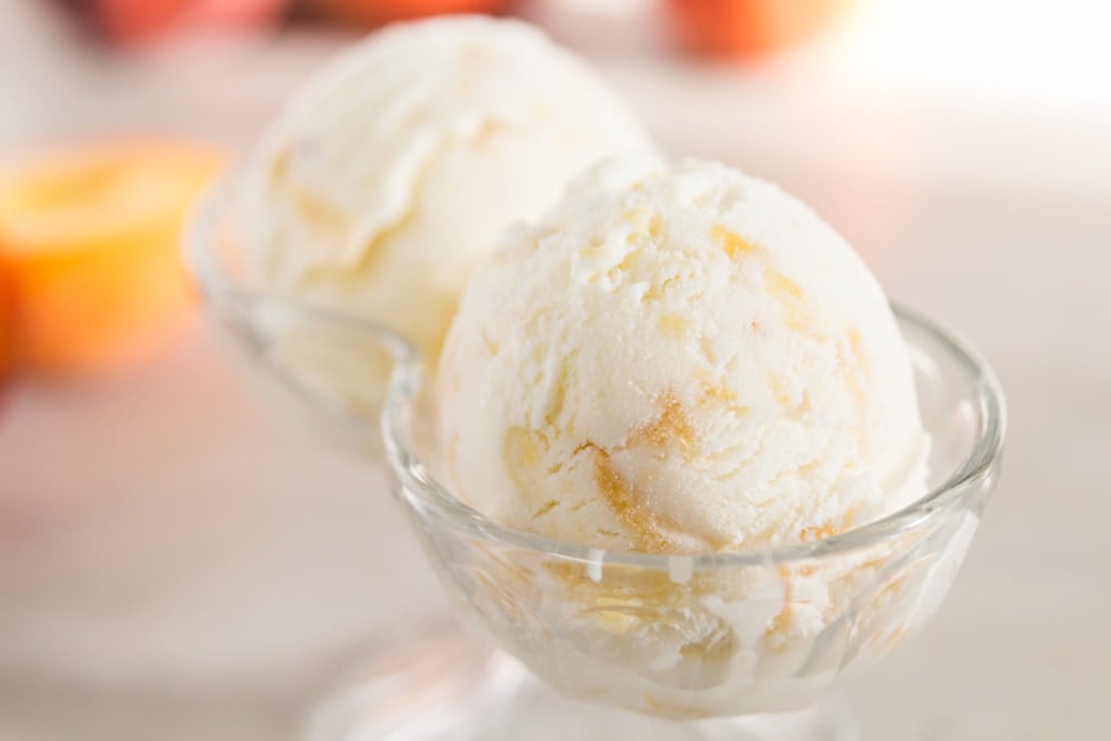 Two scoops of peach frozen yogurt sit in a glass decorative dish.