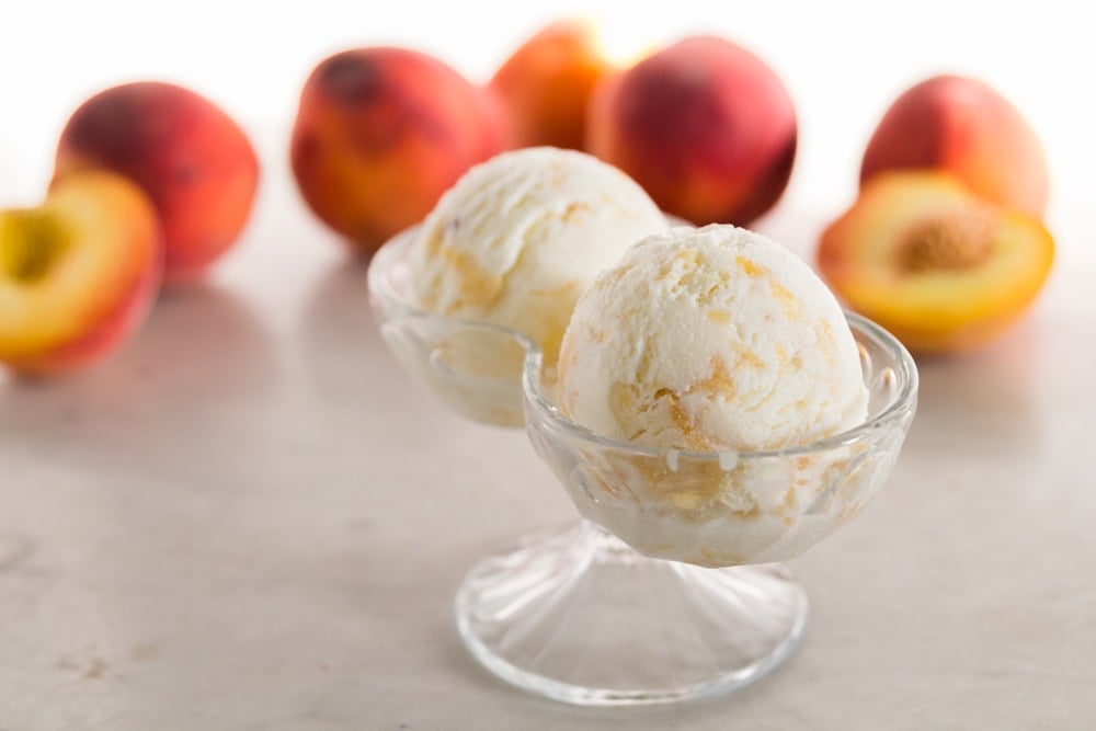 Peaches sit behind peach frozen yogurt in a glass dish.