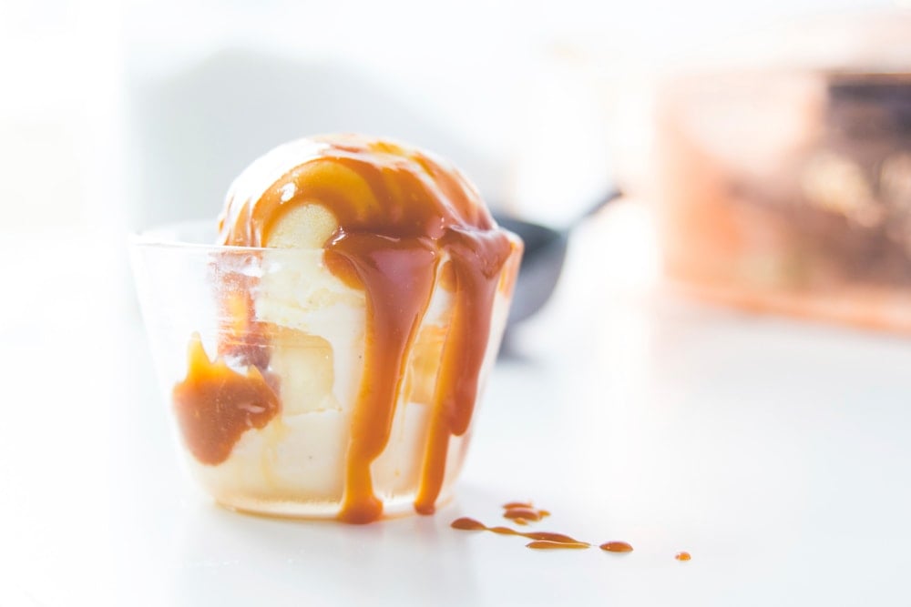 Caramel flows off a scoop of ice cream and drips on a table.