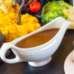 Gravy sits in a decorative dish on a dining table.