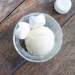 A scoop of ice cream sits next to marshmallows in a glass dish.