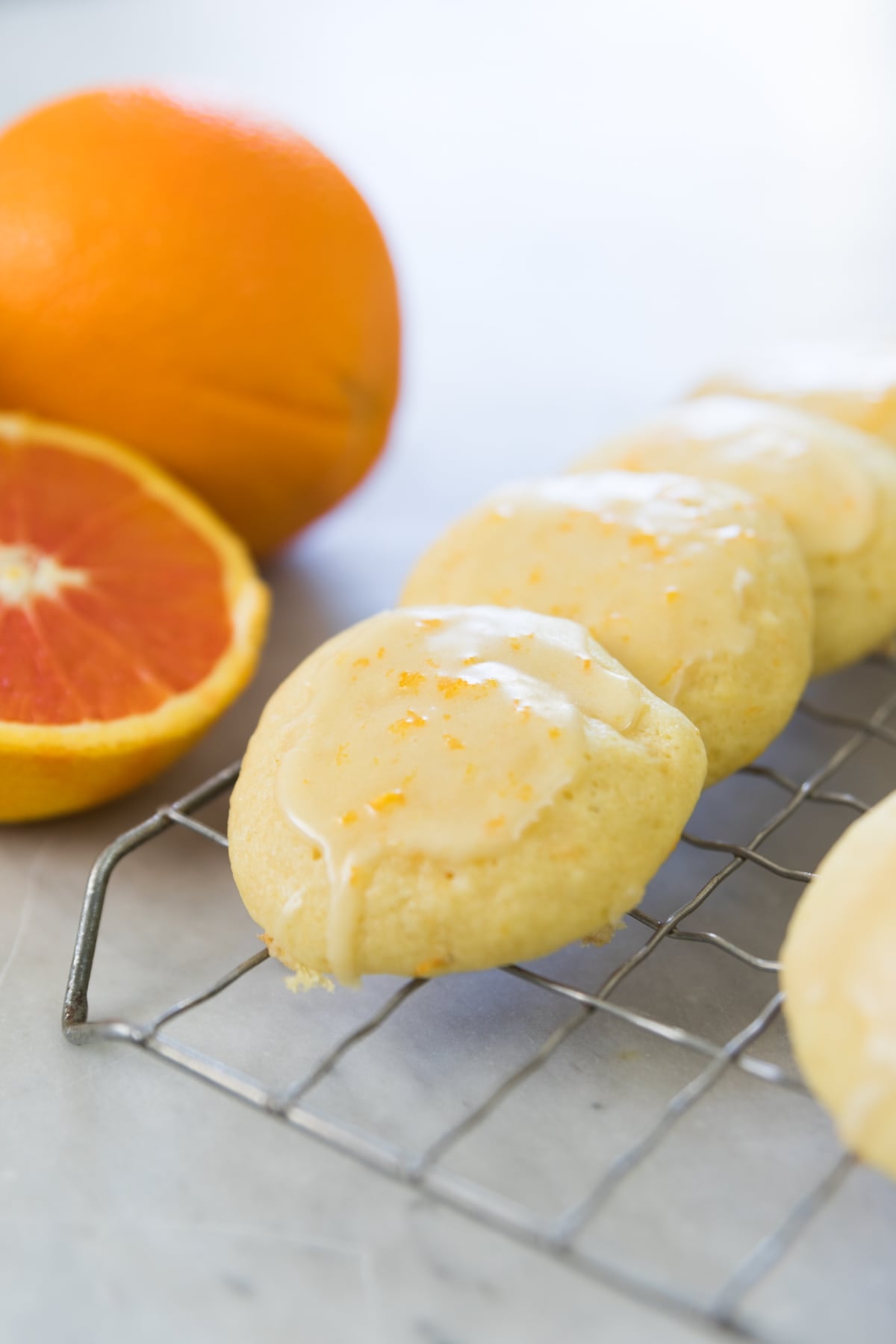 Cookies line a cooling rack on a counter in front of sliced oranges.