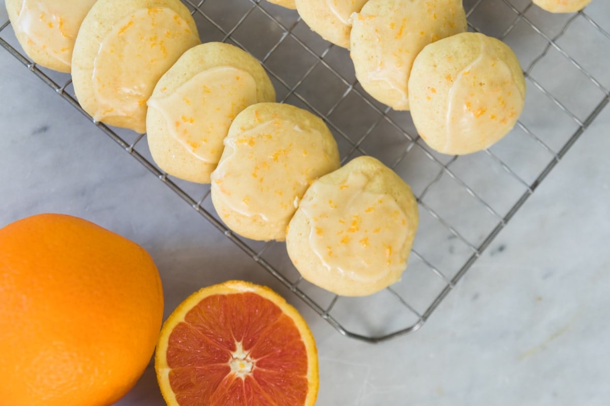 A top-down view of cookies on a cooling rack next to oranges.