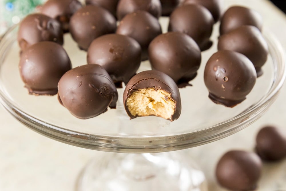 A half-eaten peanut butter truffle sits on a platter with other truffles.