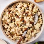 Large white bowl filled with pecan and apple chicken salad tossed with a creamy dressing along with dried cranberries.