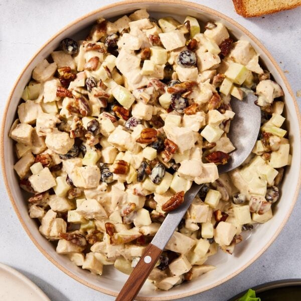 Large white bowl filled with pecan and apple chicken salad tossed with a creamy dressing along with dried cranberries.