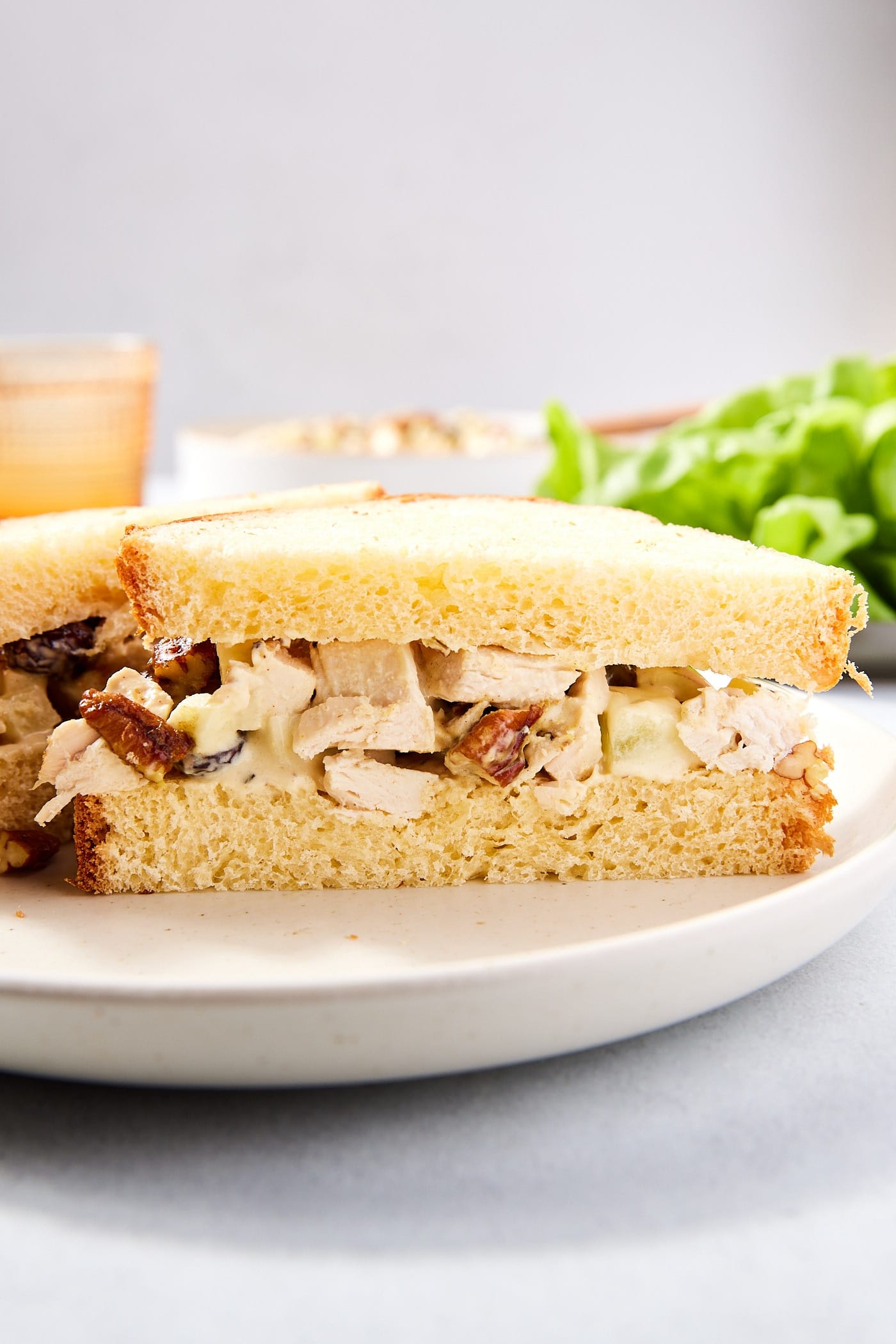 Sliced sandwich with apple chicken salad in the middle with lettuce and more chicken salad in the background.