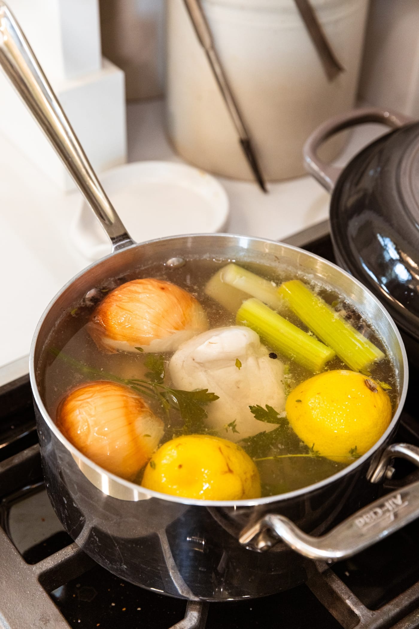 Large kettle on the stovetop filled with poached chicken and water with aromatics.