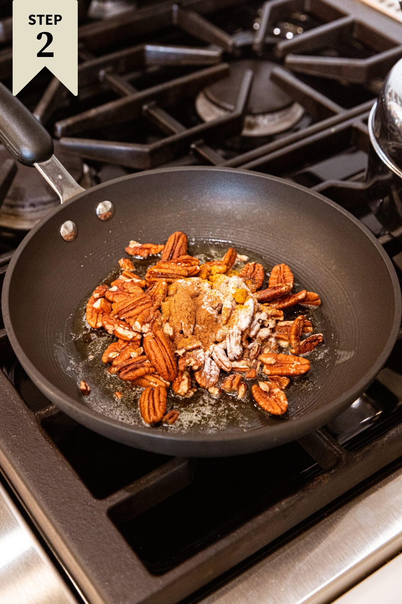 Black skillet on the stovetop filled with uncooked pecan halves and topped with sugar and spices.