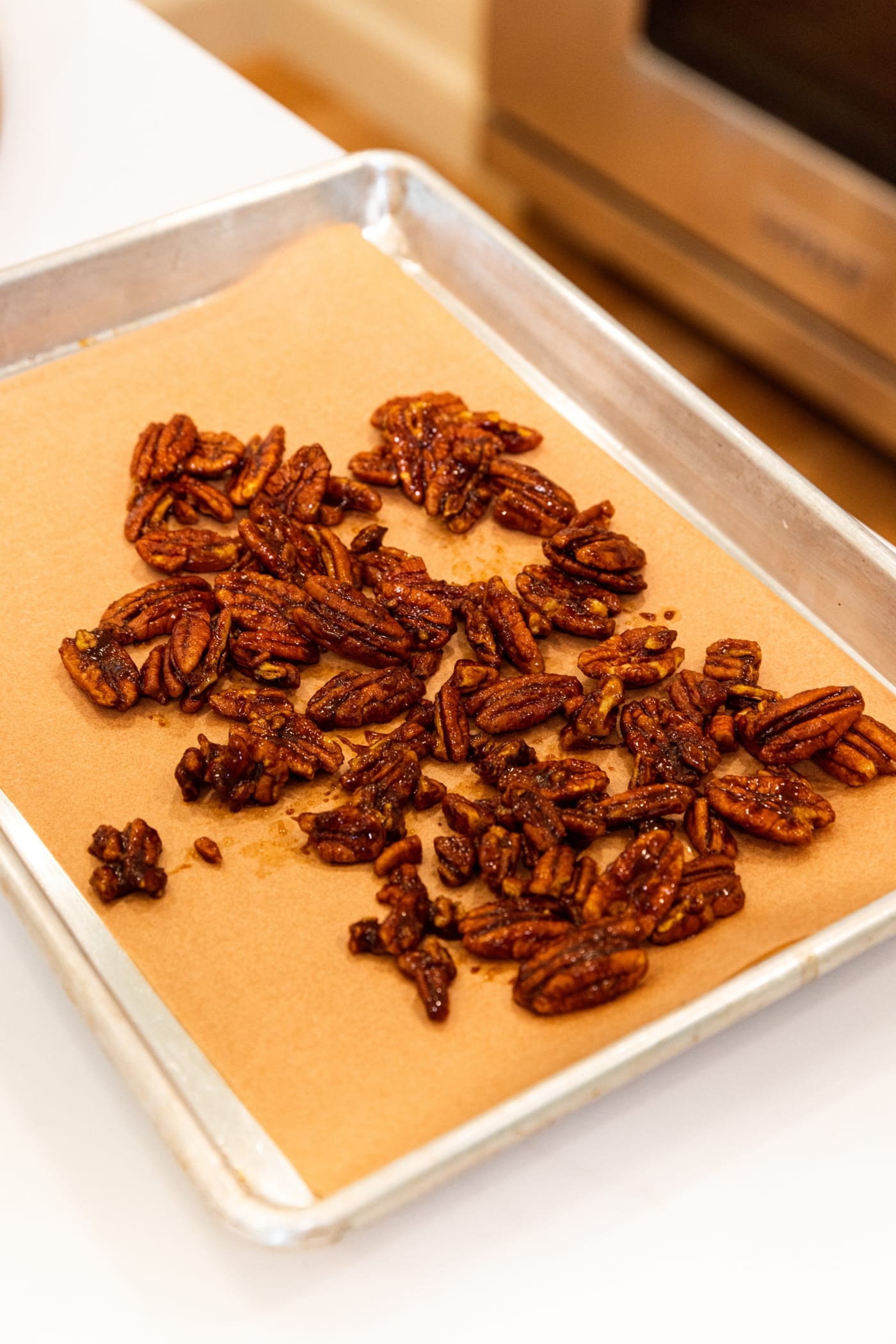 Piece of brown parchment paper with candied pecan halves cooling on top.