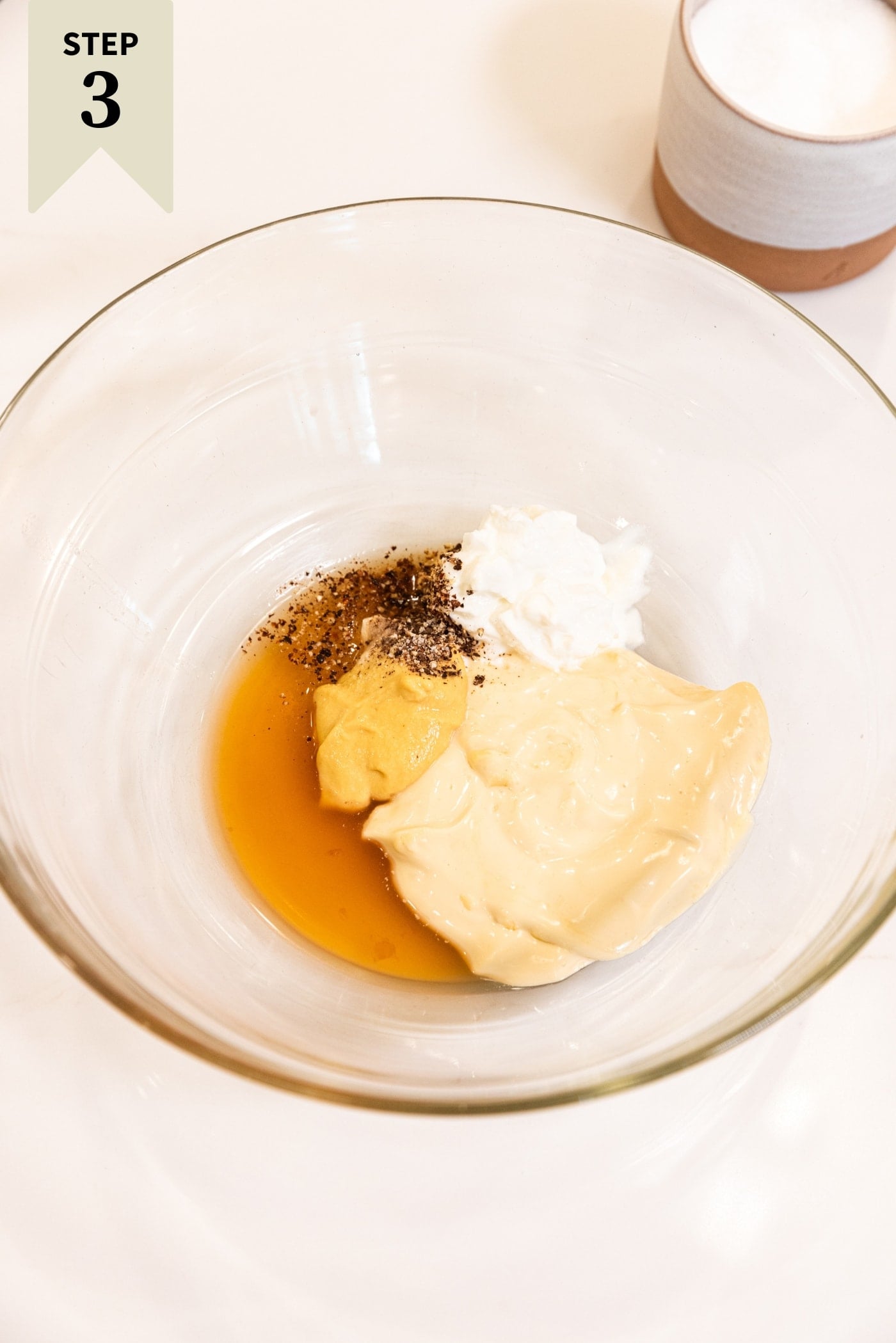 Glass bowl filled with all ingredients needed to make a quick dressing including mayonnaise, maple syrup, spices, and more.