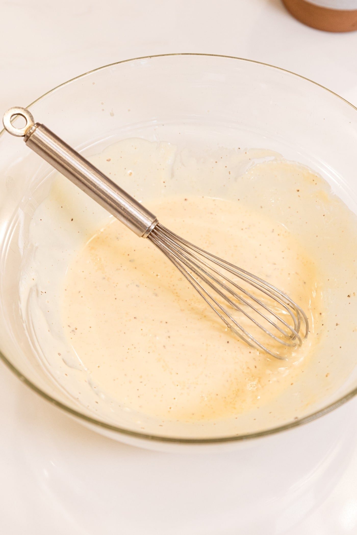 Mayonnaise-based dressing mixed together with whisk resting against the side of the bowl.