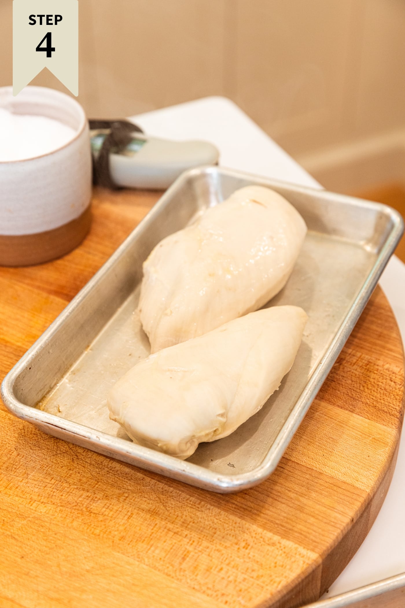 Poached pieces of chicken breast resting on a metal tray on a wooden cutting board.