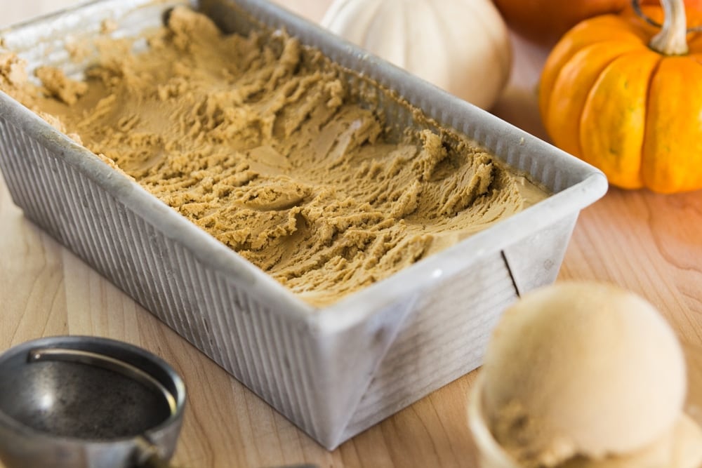 A large container full of pumpkin ice cream sits in front of small pumpkins.