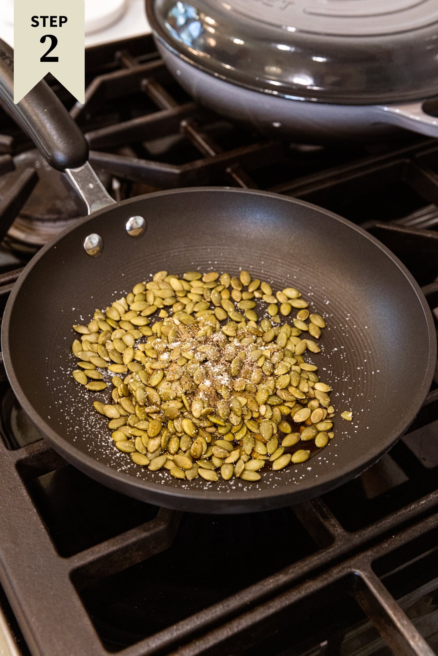 Raw pumpkin seeds sitting in roasting pan with maple syrup and salt and black pepper cooking on the stovetop.