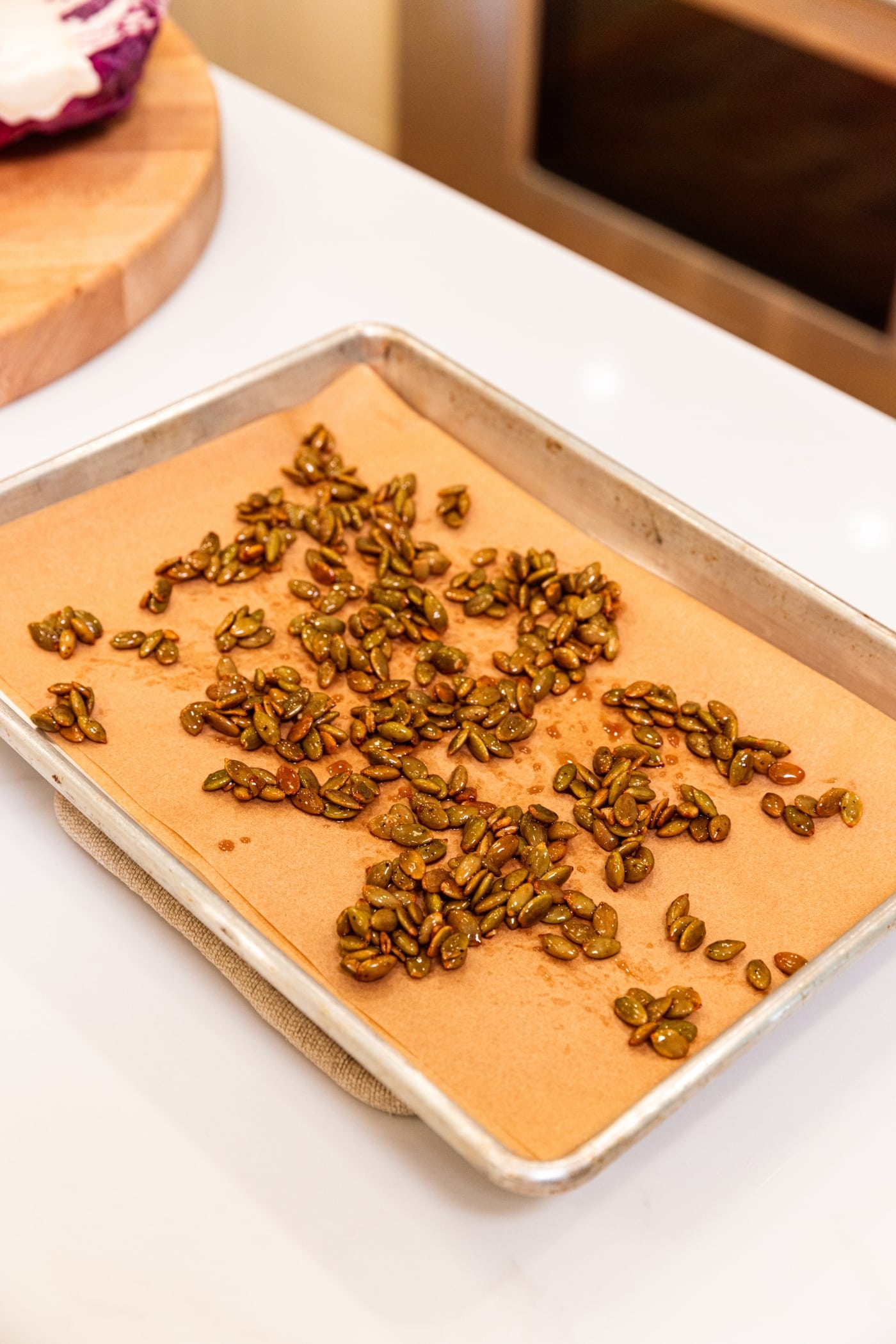 Piece of parchment in baking pan with cooling pumpkin seeds after cooking on the stovetop.