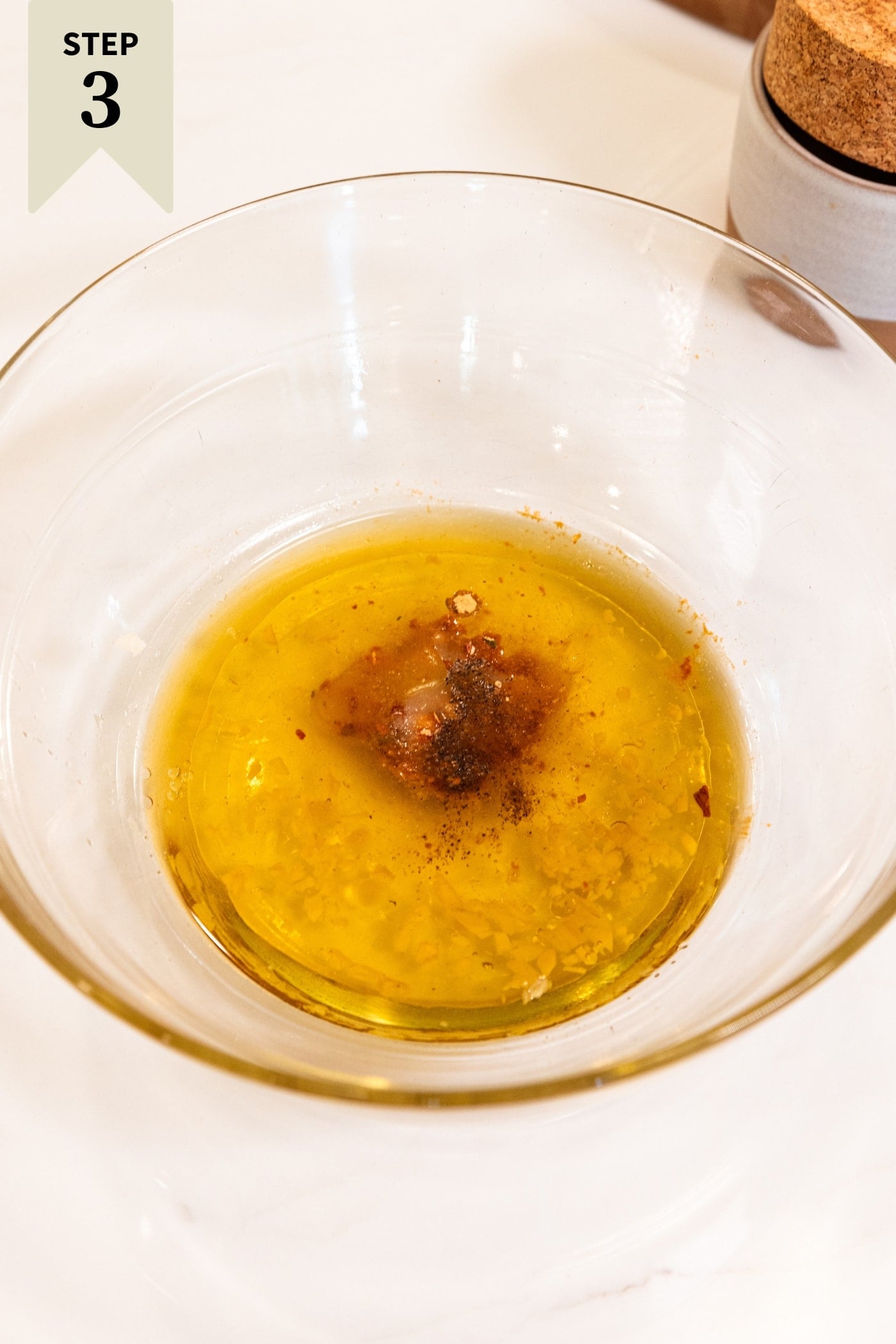 Glass bowl filled with oil and spices to make a homemade dressing for ramen chicken salad.