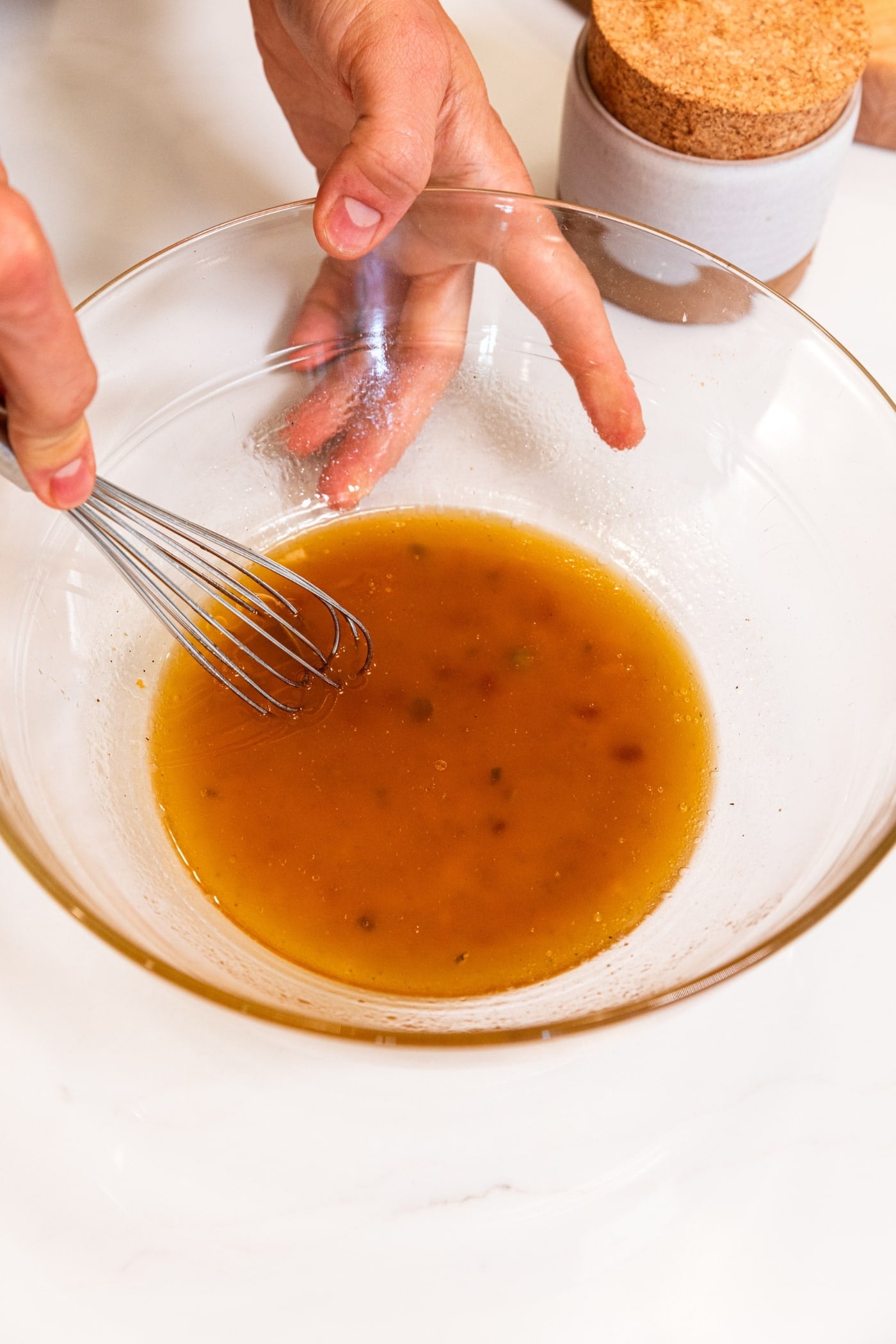 Glass bowl with dressing inside with hand stirring everything together before assembling ramen chicken salad.