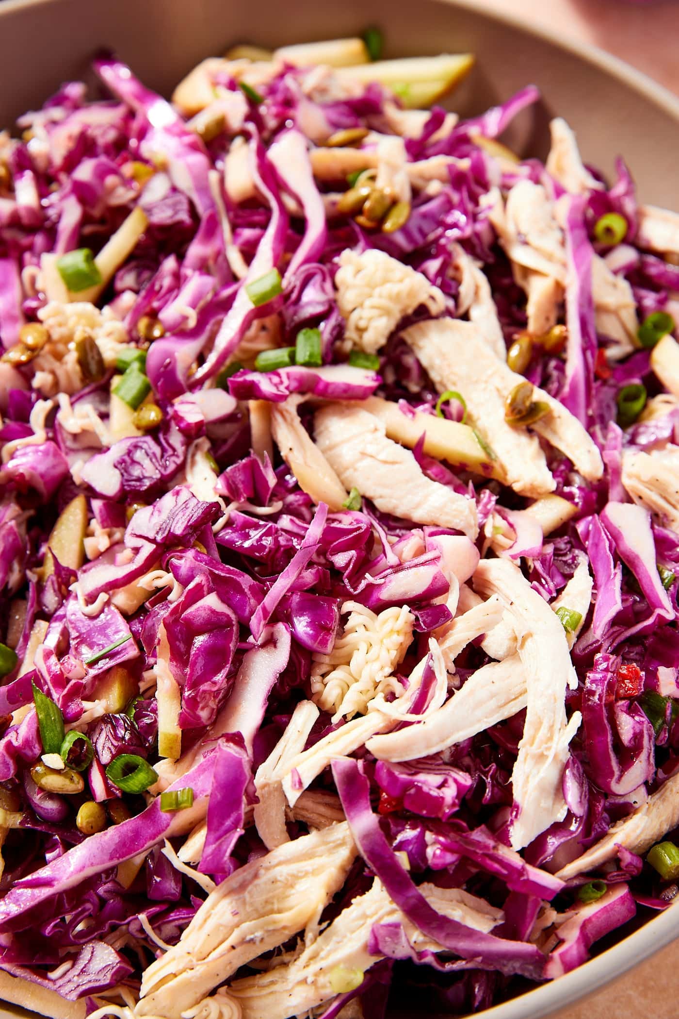 Large bowl filled with ramen chicken salad with purple cabbage and pieces of shredded roasted chicken and topped with green onion.
