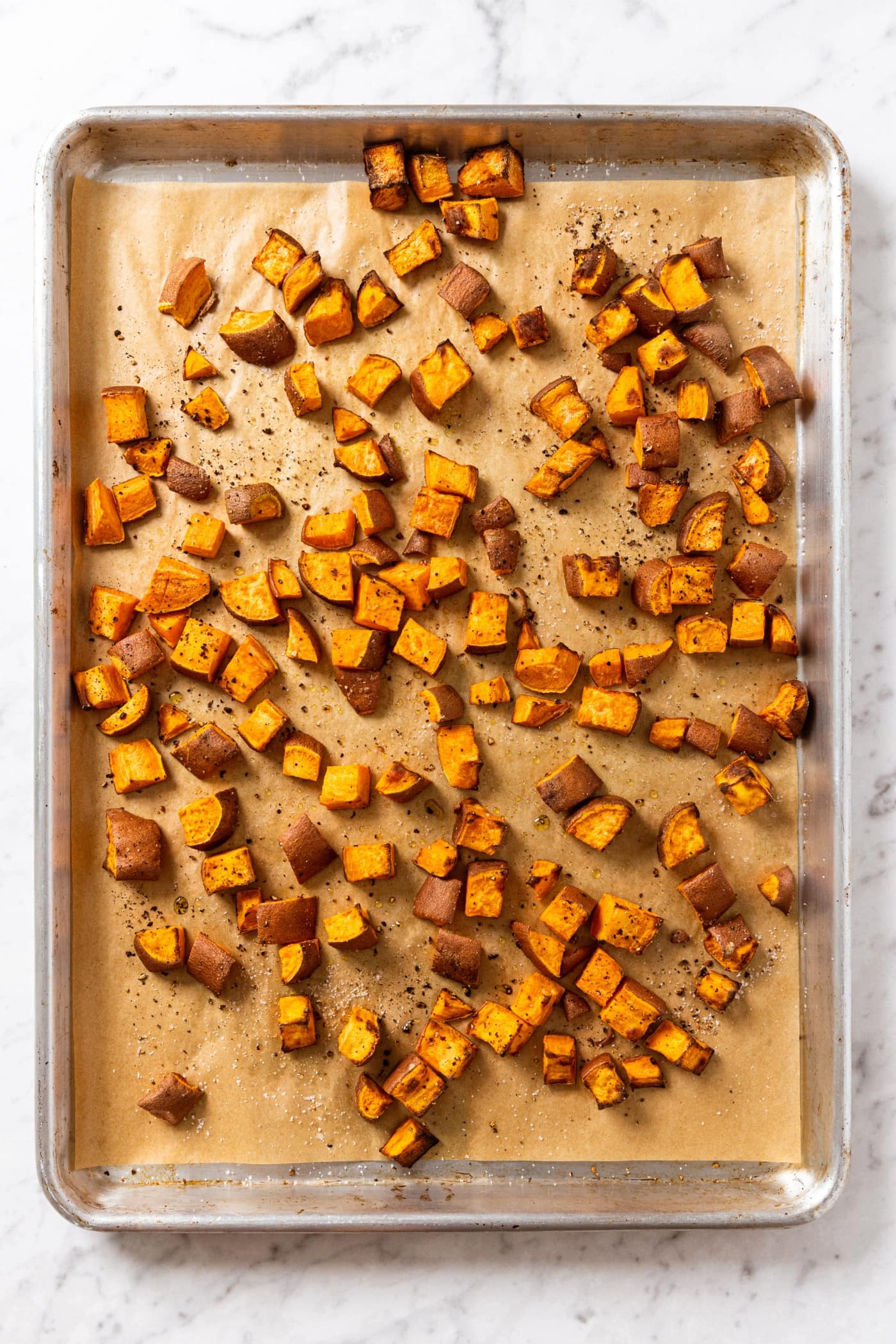 Roasted sweet potato pieces sitting on a parchment-lined baking sheet after coming out of the oven.