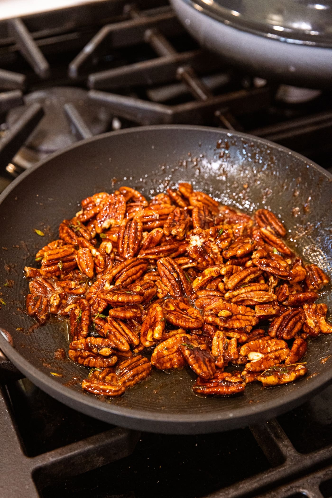Pecan halves cooking in a skillet on the stovetop in syrupy liquid.