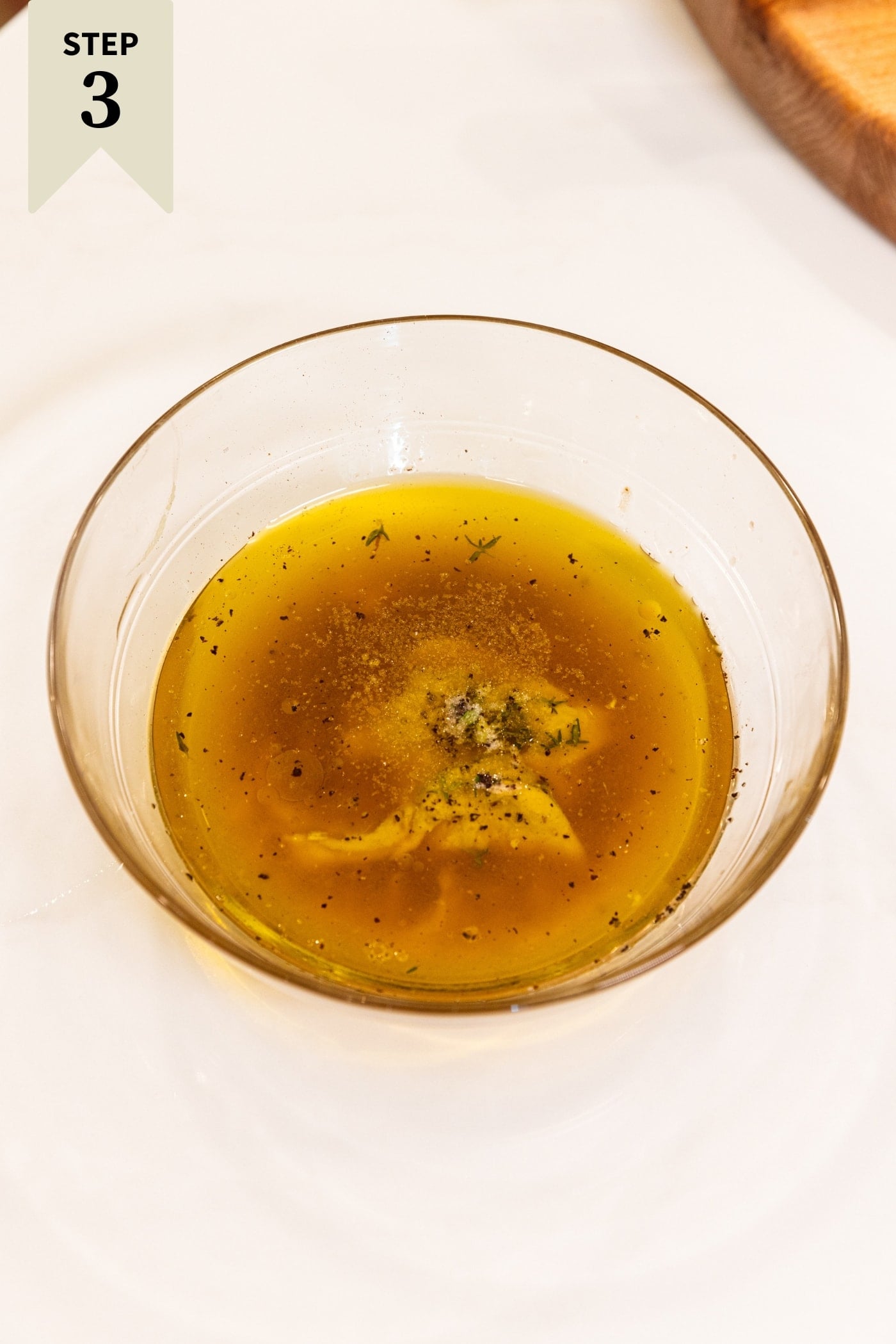Glass bowl filled with ingredients needed to make a dressing including olive oil, garlic, spices, and more.
