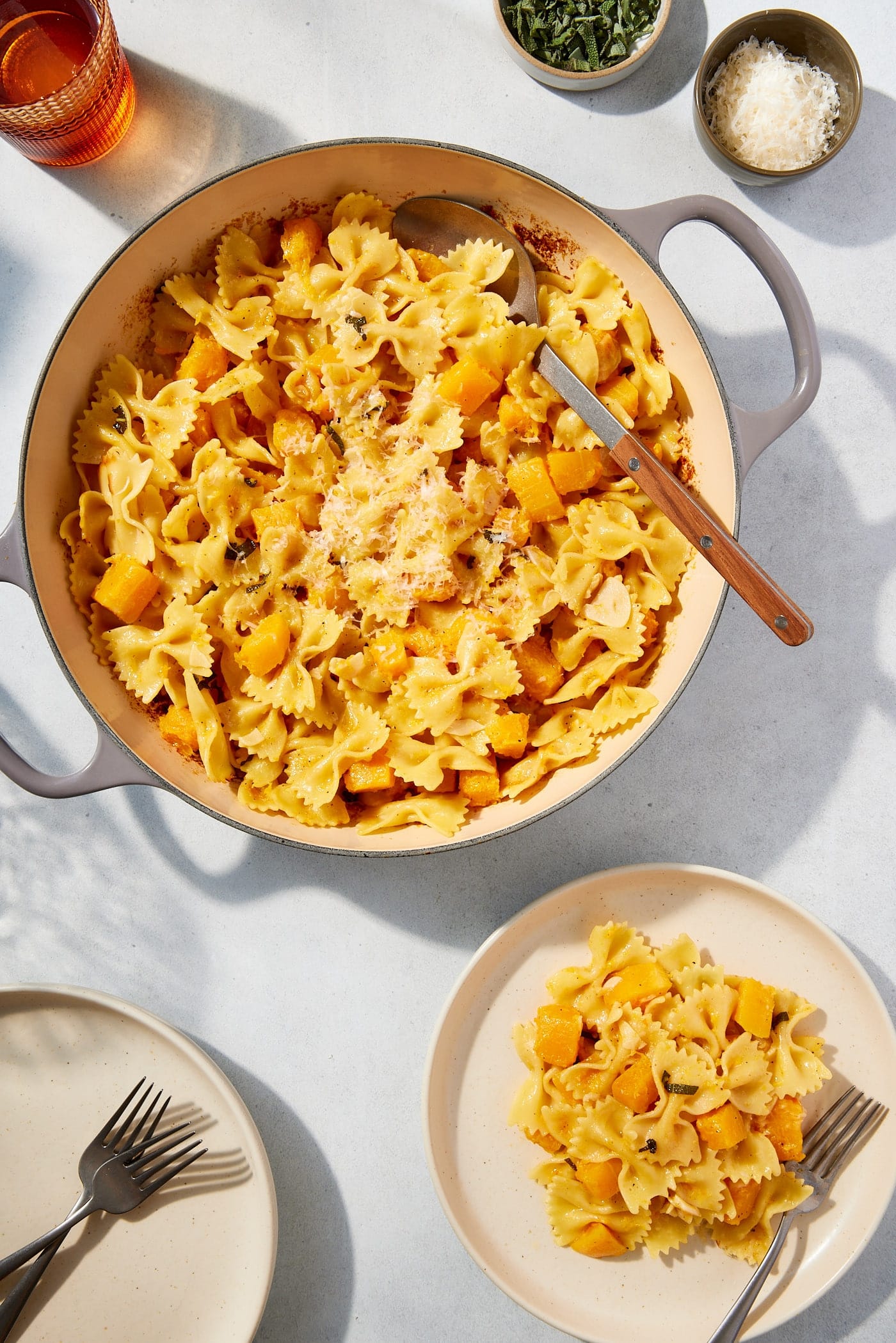 Large pot filled with cooked browned butter squash pasta with serving on a white plate with spoon resting against the side of the pot.