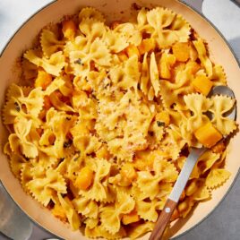 Large pot filled with cooked pasta and butternut squash with spoon resting against the side of the pot.