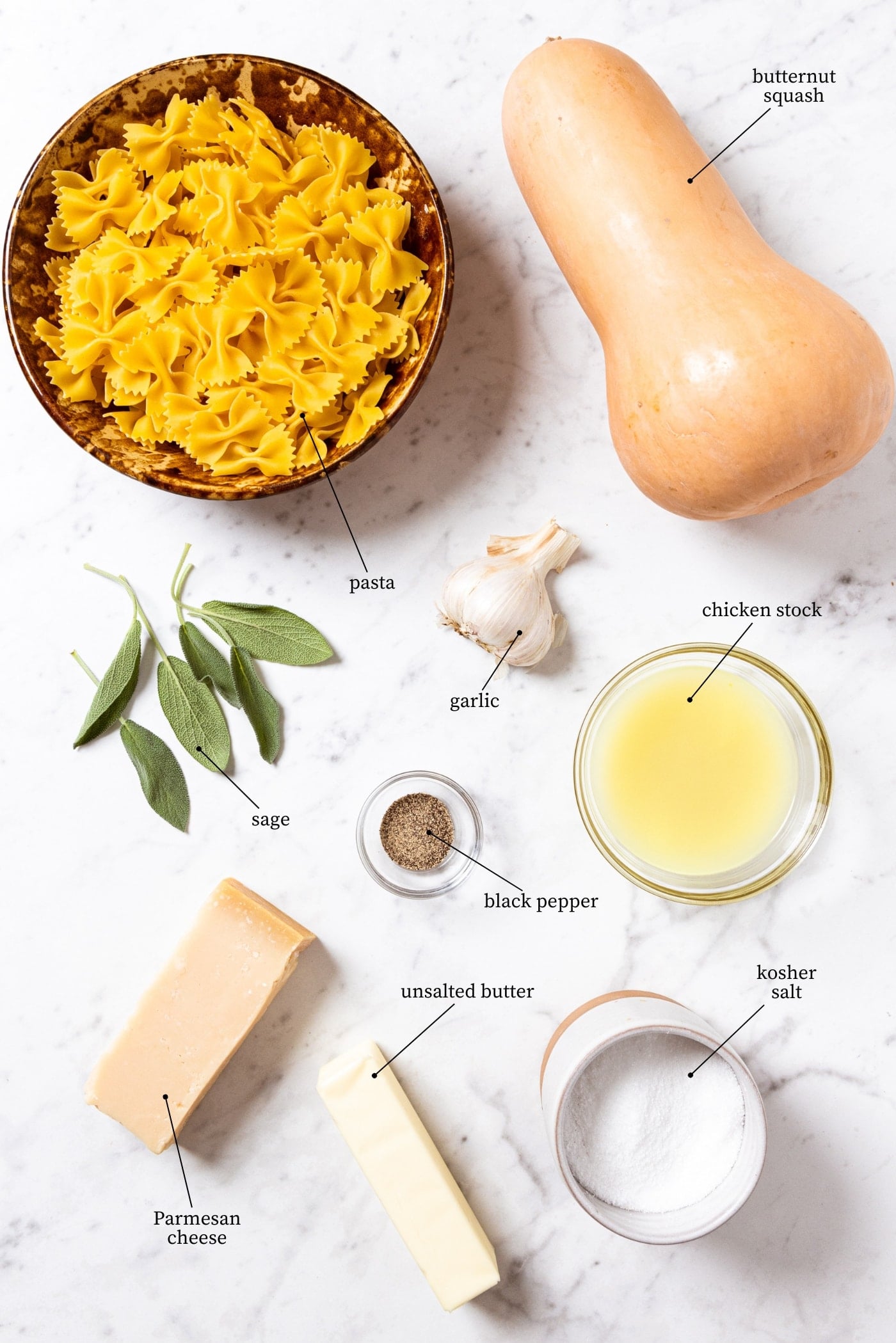 White marble surface filled with all ingredients needed to make browned butter squash pasta including pasta, squash, herbs, chicken stock, garlic, spices, and more.