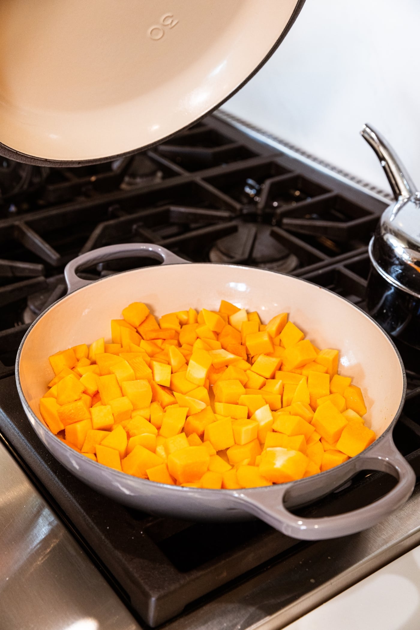 Large gray skillet resting on stovetop with cubed butternut squash before being cooked.